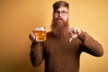 Irish redhead man with beard drinking a glass of refreshing beer over yellow background with angry face, negative sign showing Royalty Free Stock Photo