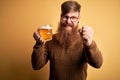 Irish redhead man with beard drinking a glass of refreshing beer over yellow background annoyed and frustrated shouting with Royalty Free Stock Photo