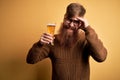 Irish redhead man with beard drinking a glass of refreshing beer over yellow background stressed with hand on head, shocked with Royalty Free Stock Photo