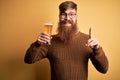 Irish redhead man with beard drinking a glass of refreshing beer over yellow background surprised with an idea or question Royalty Free Stock Photo