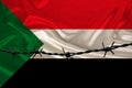 Iron barbed wire against the background of the national silk flag of the state of Sudan, concept of imprisonment for offenders,