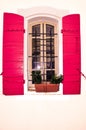 Iron barred, tall pair of windows with open red , wood shutters