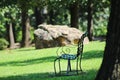 Iron bench in shade in park among large trees with giant rock in the background selective focus - bokeh Royalty Free Stock Photo