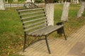 Iron bench with wooden slats in early autumn in the park near the road. Nearby is a black iron trash can Royalty Free Stock Photo