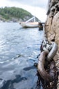 Iron chain on old stone pier, sea waves and moored sailboat and rocky shore out of focus. Bottom view. Royalty Free Stock Photo