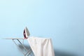 Iron and a clothes on an ironing board on a colored background. Royalty Free Stock Photo