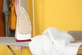 Iron and a clothes on an ironing board on a colored background. Royalty Free Stock Photo