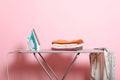 Iron and a clothes on an ironing board on a colored background. Royalty Free Stock Photo