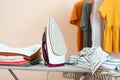 Iron and a clothes on an ironing board on a colored background. Royalty Free Stock Photo