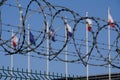 Iron fence and barbed wire on a blured background of white-red. white-blue flags and blue sky on a Sunny day. Polish border Royalty Free Stock Photo