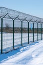 Iron fence with barbed wire in a snow-covered winter field against a blue sky. Fenced guarded territory, no access. Area Royalty Free Stock Photo