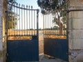 Iron gate with a small opening to let a person with visible narrow path through the opening.