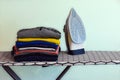 Modern iron on ironing board and a pile of clean and tidy clothes Royalty Free Stock Photo