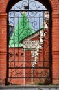 Iron koala gate with a cross behind which is a red brick wall. Russia Yoshkar-Ola 01.05.2021