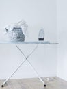 Iron and laundry basket on ironing board against white wall Royalty Free Stock Photo