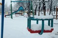 Iron metal children's kids swing playground. Slide in the background. Empty playground is covered in snow. Royalty Free Stock Photo