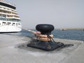 Iron mooring bollard in port with rope and moored cruise ship. Bow of Cruise Ship Tied to Black Bollard with thick rope. Cruise Royalty Free Stock Photo