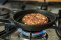 Iron pan with raw cutlet on a gas stove