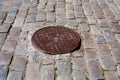 Iron rusty manhole cover on an old cobblestone road. Royalty Free Stock Photo