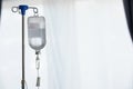 An iron stand to hang saline bottle high to deliver saline via catheter to an intravenous patient lying on patient bed. Medical
