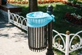 Iron trash urn with one-time package inside on the background of benches, fences and flowers in sunny park Royalty Free Stock Photo