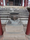 Iron vessel with Japanese writing used for burning incense. In the background stairs, iron door, brown posts in a Buddhist temple