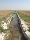 Irrigation canal flowing through flatlands bordered by stone banks on a sunny day Royalty Free Stock Photo