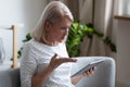 Irritated aged woman holding broken tablet having problems with gadget