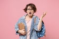 Irritated angry young woman student in denim clothes eyeglasses backpack isolated on pastel pink background. Education