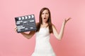 Irritated bride woman in white wedding dress swearing spreading hand holding classic black film making clapperboard