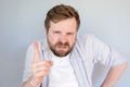 Irritated, disgruntled bearded man looks evil and threatening gesture with his finger. Gray background.