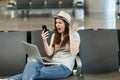 Irritated dissatisfied traveler tourist woman with laptop hold mobile phone spread hands wait in lobby hall at
