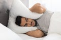 Irritated young arab man lying in bed and covering head with pillow Royalty Free Stock Photo