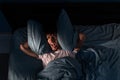 Irritated young man laying in bed at night, covering his head with pillows, stress from noise, sleepless guy having Royalty Free Stock Photo