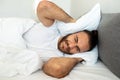 Irritated young man lying in bed, covering head with pillow Royalty Free Stock Photo