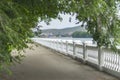 Irtysh River Embankment Seen Through the Tree Crown Arch with Blurred Dockside Cranes, Apartment Blocks, Houses, and Mountains on