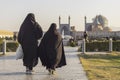 Two women in black chadors walk in Imam Square. The Shah Mosque on the background. Back view