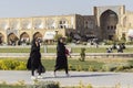 Two young Iranian girls in black chadors walk in Imam Square. Sheikh Lotfollah Mosque on the background