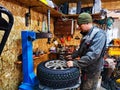 Ishim, Russia - November 27, 2023: A mechanic repairs a car wheel and makes a tire in a dirty garage. Replacement of