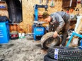 Ishim, Russia - November 27, 2023: A mechanic repairs a car wheel and makes a tire in a dirty garage. Replacement of