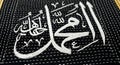 Close up view of islamic calligraphy embroidery on black fabric prayer mat with white threads displaying religious script in Royalty Free Stock Photo