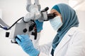 Islamic dentist woman wearing protective medical mask using dental microscope in clinic