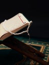 Islamic Holy Book Quran on wood carving rahle with rosary beads and prayer rug on black background. Kuran the holy book of Muslims