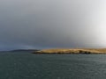The Isle of Bressay with its Grass and heather covered land lit up by the Winters sun under the dark clouds of a Winters Storm