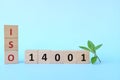 ISO 14001 or Environmental Management System on wooden blocks in blue background with green leaf.