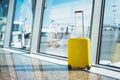 Isolate traveler tourist yellow suitcase at floor airport on background large window, bright luggage waiting in departure lounge Royalty Free Stock Photo