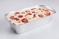 Isolated close corner view of a Russian zapekanka strawberry pudding cottage ice cream cheese cake in a foil baking pan on a white