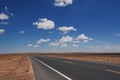 Isolated desert highway stretching out into the horizon, surrounded by lush clouds