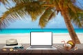 Isolated display of laptop on wooden table for mockup. Beach, sea, palm and blue sky in background. Royalty Free Stock Photo