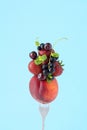 Isolated fruit stack with peach, strawberry, cherry, gooseberry and black currant on fork on blue